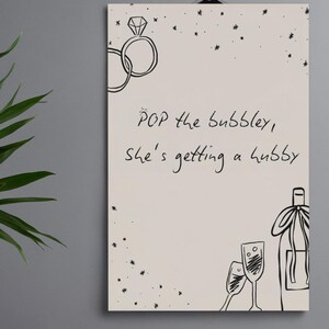 Pode incluir: Uma placa de parede retangular com fundo bege claro apresentando desenhos de linhas pretas de dois anéis de diamante entrelaçados, uma garrafa de champanhe e duas taças. O texto diz: POP the bubbley, she's getting a hubby, rodeado por pequenas estrelas.