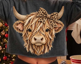 May include: A charcoal gray long-sleeve cropped sweatshirt featuring a large graphic of a Highland cow with a leopard print bow between its horns. The cow has shaggy light brown fur and prominent horns, centered on the front of the garment.