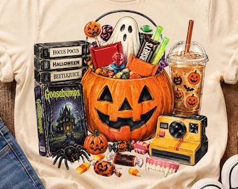 May include: A cream-colored t-shirt featuring a graphic print of a jack-o'-lantern bucket filled with candy, a ghost, and a drink. Beside it are stacked VHS tapes labeled Hocus Pocus, Halloween, Beetlejuice, and Goosebumps, plus a yellow camera.