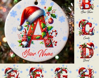May include: A round white ceramic ornament featuring a large red letter A decorated with holly, berries, and a gnome wearing a Santa hat. The design includes blue snowflakes and the text Your Name in red script at the bottom.