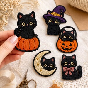 May include: Five embroidered patches featuring black cats. One cat sits on an orange pumpkin, one wears a purple witch hat, one sits in a jack-o'-lantern bucket, one rests inside a gold crescent moon with stars, and one wears a pink bow tie.