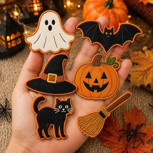 Könnte beinhalten: Ein Set aus sechs bestickten Halloween-Aufnähern, bestehend aus einem weißen Geist, einer schwarzen Fledermaus, einem schwarzen Hexenhut mit goldener Schnalle, einem orangefarbenen Kürbis, einer schwarzen Katze und einem braunen Besen mit Stickerei.