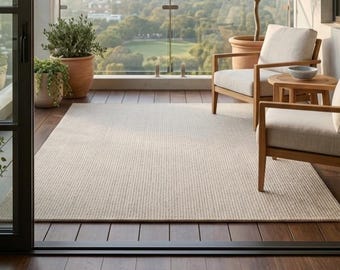 May include: A rectangular area rug with a light beige and white fine-ribbed texture, positioned on a dark brown wooden deck. The rug is surrounded by two wooden armchairs with off-white cushions, a small round side table, and potted plants.