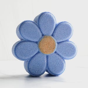 Op de afbeelding: Een bloemvormige bruisbal met een getextureerd, lichtblauw oppervlak dat zes afgeronde bloemblaadjes en een cirkelvormig, bruinachtig centrum vormt. Het object heeft een solide, geperste uitstraling met gedefinieerde randen en een matte afwerking.