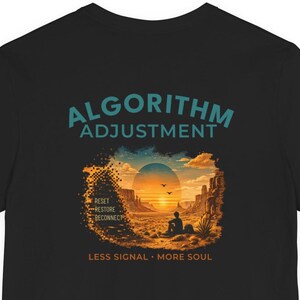 May include: A black t-shirt featuring the teal text ALGORITHM ADJUSTMENT at the top. Below, a graphic shows a desert landscape at sunset with a person sitting, the words RESET RESTORE RECONNECT, and the text LESS SIGNAL MORE SOUL at the bottom.