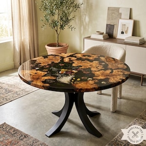 May include: A round dining table featuring a polished surface with embedded natural wood burl sections and a central arrangement of dried flowers encased in dark resin, supported by a black metal base with four curved legs.