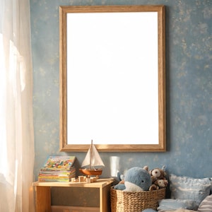Puede incluir: Un marco de fotos rectangular de madera con un centro blanco vacío, montado en una pared azul. Debajo del marco hay una mesa de madera con una pila de libros y un modelo de velero, junto a una cesta tejida llena de peluches.