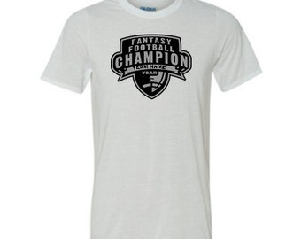 May include: White t-shirt with a black graphic that says "Fantasy Football Champion" with a football and shield design. The graphic also includes the text "Team Name" and "Year".