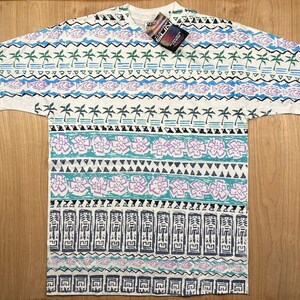 May include: A white short-sleeve t-shirt featuring a repeating horizontal pattern of palm trees, fish, flowers, and geometric shapes in shades of blue, purple, green, and black. A rectangular tag labelled THERMAL SUN is attached to the collar area.