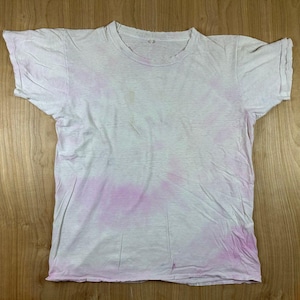 May include: A short-sleeved crew neck t-shirt featuring a subtle tie-dye pattern in shades of white and pale pink. The garment has a standard fit with a rounded neckline and hemmed sleeves, showcasing a soft, washed-out aesthetic throughout.