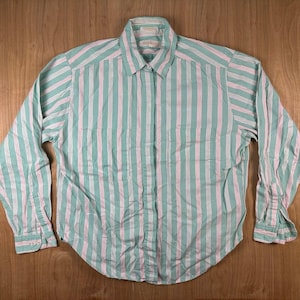 May include: A long-sleeved button-down shirt featuring a vertical striped pattern in shades of mint green, white, and soft pink. The shirt includes a standard collar, a front button placket, and buttoned cuffs on the sleeves, with a curved hemline.