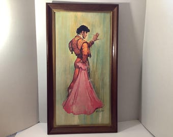 May include: A framed painting of a bullfighter wearing an ornate gold and orange jacket, holding a large pink cape. The figure stands in profile against a pale green background. The artwork is enclosed in a dark brown wooden frame.