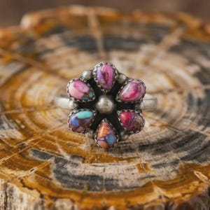 May include: A silver ring featuring a flower-shaped cluster of six teardrop-shaped stones. The stones display a variety of colors including shades of pink, purple, orange, and turquoise with dark matrix veining. A central silver bead sits in the middle.