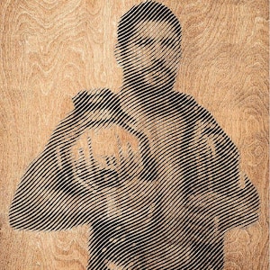May include: A rectangular wooden plaque featuring a black line-art portrait of a person in a fighting stance. The artwork is created with horizontal black lines on a natural light brown wood grain background. The text UFC WHITE HOUSE is printed in black.
