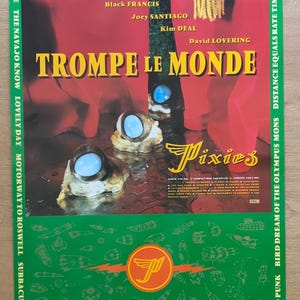 Puede incluir: Un póster musical rectangular para el álbum Trompe le Monde de Pixies. El diseño presenta un fondo rojo con tres esferas azul claro sobre bases texturizadas, el nombre de la banda, la lista de canciones y un borde verde con cohetes.