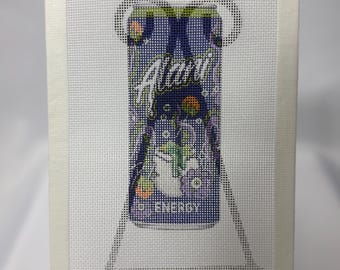 May include: A needlepoint canvas featuring a graphic design of an Alani energy drink can. The can is purple with white text that reads Alani and ENERGY, accented with colorful circular bubbles and abstract shapes on a white mesh grid background.