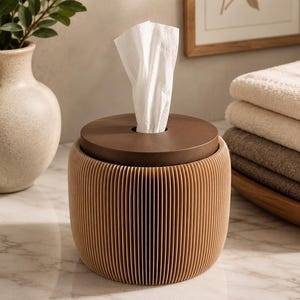 May include: A cylindrical tissue box cover featuring a light tan, vertically ribbed exterior body and a smooth, flat, dark brown circular lid with a central opening through which a single white tissue is pulled upward for easy access.