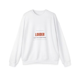 Peut inclure: Un sweat-shirt blanc à manches longues et col rond avec un texte centré indiquant LOUDER THAN ANY SUPER BOWL, accompagné de lignes de texte plus petites au-dessus et en dessous de la phrase principale dans une police simple et épurée.