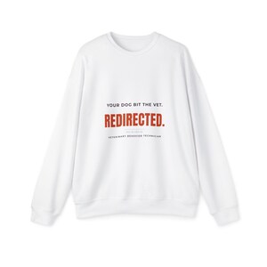 May include: A white long-sleeve crewneck sweatshirt featuring black and red text on the front. The text reads: YOUR DOG BIT THE VET. REDIRECTED. VETERINARY BEHAVIOR TECHNICIAN. The garment has a ribbed collar, cuffs, and a straight hemline.
