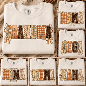 Könnte beinhalten: Ein cremefarbenes Sweatshirt mit Rundhalsausschnitt, das das Wort GRANDMA in großen Blockbuchstaben mit verschiedenen Mustern wie orangefarbenem Vichy-Karo, Leopardenmuster, Blumen und Punkten zeigt, verziert mit dekorativen Schleifen.