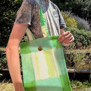 Könnte beinhalten: Eine rechteckige Tragetasche mit einem Blockdruckmuster in den Farben Limettengrün, Waldgrün und Weiß. Die Tasche verfügt über zwei Stoffschulterriemen und einen einzelnen runden braunen Knopf, der mittig nahe der oberen Kante angebracht ist.
