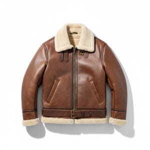 Puede incluir: Una chaqueta tipo aviador de cuero marrón con cuello y puños de borreguillo color crema. La prenda incluye un cierre de cremallera frontal, dos bolsillos laterales y un cinturón con hebilla en la cintura. Dos correas con hebilla están en el cuello.