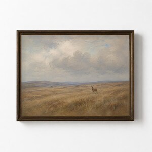 May include: A framed landscape painting depicting a solitary deer standing in a vast, golden-brown grassy field under a cloudy, overcast sky. The scene features rolling hills in the distance and is enclosed in a dark brown wooden frame.