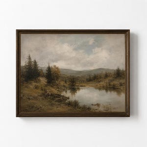 Puede incluir: Un cuadro de paisaje enmarcado que representa un lago tranquilo rodeado de pinos de color verde oscuro y colinas bajo un cielo nublado y apagado. La obra presenta tonos tierra de marrón, verde y gris, en un marco de madera marrón oscuro.