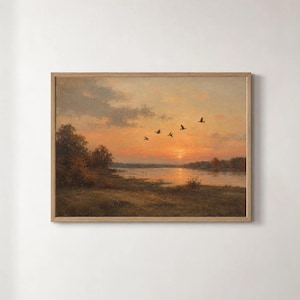 Può includere: Un dipinto di paesaggio rettangolare in una cornice di legno chiaro che raffigura un tramonto su un fiume calmo. Il cielo è pieno di tonalità arancioni e gialle, con un piccolo stormo di uccelli che vola sopra l'acqua e gli alberi scuri.