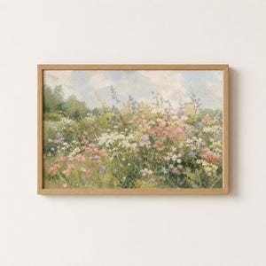 Pode incluir: Uma pintura de paisagem retangular numa moldura de madeira clara que retrata um prado exuberante cheio de flores silvestres em tons de rosa, branco e azul. A cena apresenta folhagem verde densa sob um céu azul pálido e nublado.