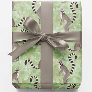 May include: A rectangular gift box wrapped in light green paper featuring a repeating pattern of grey and white lemurs with long striped tails. The package is tied with a smooth, solid grey satin ribbon that is knotted into a decorative bow.