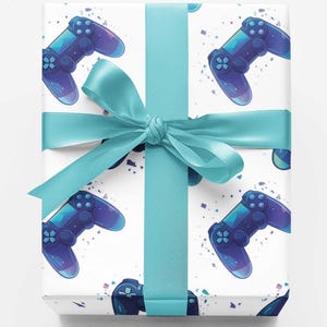 May include: A rectangular gift box wrapped in white paper featuring a repeating pattern of blue video game controllers and small confetti-like shapes. The package is tied with a wide, smooth, light blue satin ribbon centered in a bow.