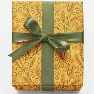May include: A rectangular gift box wrapped in yellow paper featuring a repeating pattern of brown wheat stalks and dark green swirling vines. The package is tied with a wide, smooth, olive green satin ribbon tied in a centered bow.