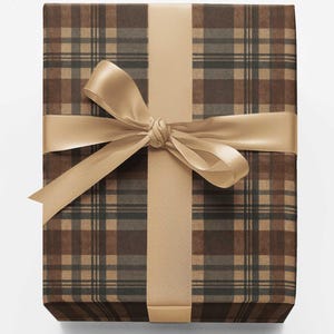 May include: A rectangular gift box wrapped in brown, tan, and dark gray plaid paper. The package is tied with a smooth, solid light tan satin ribbon that forms a decorative bow centered horizontally across the front of the wrapped box.