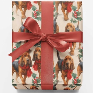 May include: A square gift box wrapped in cream-colored paper featuring a repeating pattern of brown and black bloodhound dogs wearing red scarves, interspersed with green holly leaves and red berries, tied with a wide red satin ribbon bow.