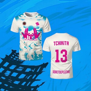 May include: A white short-sleeve t-shirt featuring a blue marbled pattern, a pink graphic of hands forming a sign above the text JUL, and a small logo on the chest. The back displays the text TCHIKITA, the number 13, and DORETDEPLATINE in pink.