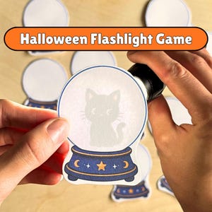 May include: A Halloween Flashlight Game set featuring paper cutouts of crystal balls. One cutout shows a black cat silhouette inside the globe, which sits on a dark blue base with a yellow star and crescent moon design. Other blank cutouts are visible.