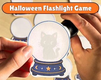 May include: A Halloween Flashlight Game set featuring paper cutouts of crystal balls. One cutout shows a black cat silhouette inside the globe, which sits on a dark blue base with a yellow star and crescent moon design. Other blank cutouts are visible.