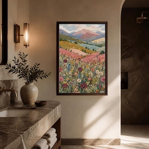 May include: A framed vertical wall art print depicting a landscape painting of rolling hills, a wildflower meadow with pink, red, and white flowers, and distant mountains under a soft sky, displayed on a beige wall above a marble bathroom vanity.