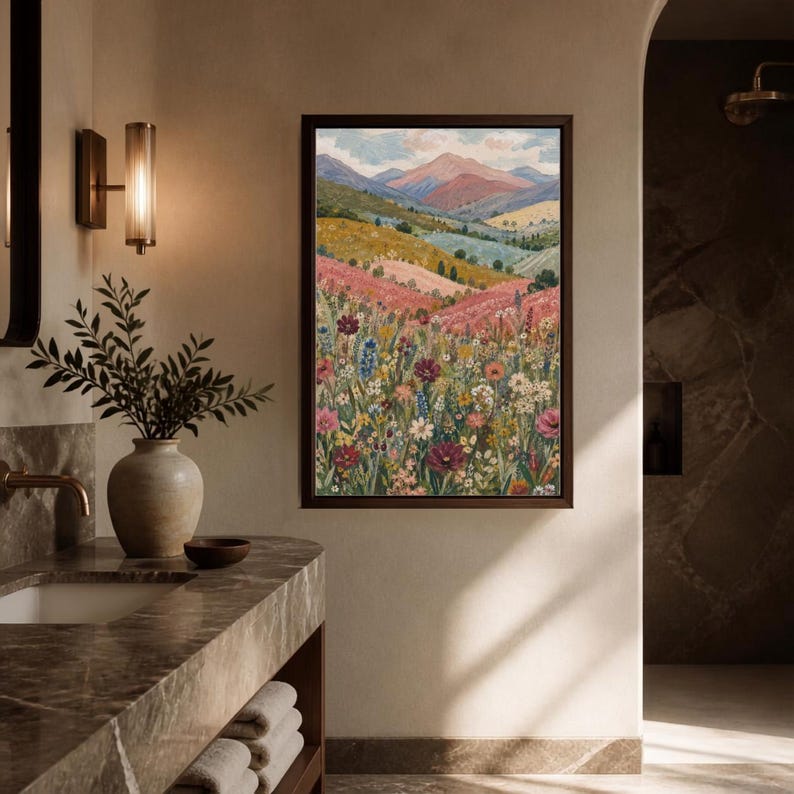 May include: A framed vertical wall art print depicting a landscape painting of rolling hills, a wildflower meadow with pink, red, and white flowers, and distant mountains under a soft sky, displayed on a beige wall above a marble bathroom vanity.