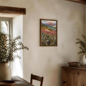 May include: A rectangular framed wall art print featuring a vibrant landscape painting. The artwork displays a foreground filled with colorful wildflowers in shades of pink, yellow, and blue, leading to rolling hills and distant mountains under a soft sky.