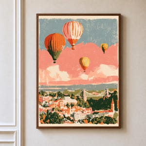 May include: A framed wall art print featuring a stylized illustration of four hot air balloons floating above a city landscape with a suspension bridge. The color palette includes shades of orange, yellow, muted blue, and cream with a textured finish.