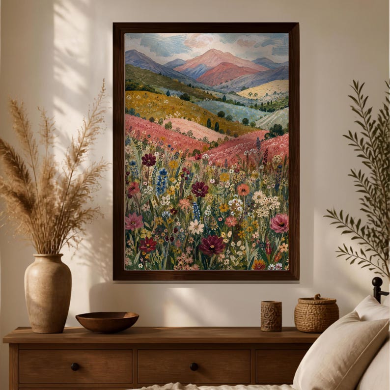 May include: A framed landscape painting featuring a vibrant wildflower meadow in the foreground with rolling hills and distant mountains under a soft sky. The artwork displays a rich palette of pink, yellow, green, and deep red floral tones.