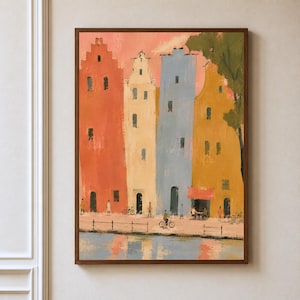 May include: A framed painting depicts a row of tall, narrow buildings in shades of orange, cream, blue, and yellow along a canal. Small figures walk and cycle on the path, while reflections of the colorful structures appear in the water below.