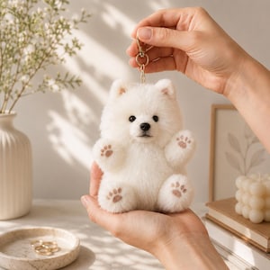 May include: A fluffy white plush dog keychain featuring a small, round body, pointed ears, and dark eyes. The plush toy has light brown paw pads on its feet and hands, and it is attached to a gold-toned metal lobster clasp for easy hanging.