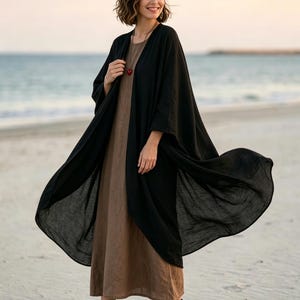 May include: A long, flowing black open-front kimono layered over a solid brown midi dress. The outfit is paired with black ankle boots featuring fringe detailing and a simple necklace with a small red heart pendant.