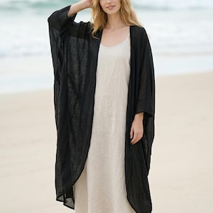 May include: A long, black, open-front kimono-style robe with wide sleeves, layered over a simple, floor-length, beige slip dress with thin spaghetti straps. Both garments feature a textured, lightweight fabric construction with a loose, flowing fit.