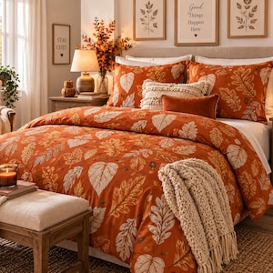 May include: A bedding set featuring a burnt orange duvet cover and matching pillow shams decorated with a white and light brown leaf pattern. The bed is styled with a cream-colored textured throw blanket and a solid orange rectangular accent pillow.