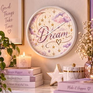 May include: A round wall clock with a white frame featuring a celestial design of a crescent moon, gold stars, and purple clouds. The word Dream is written in cursive script across the center. The clock has white hour, minute, and second hands.