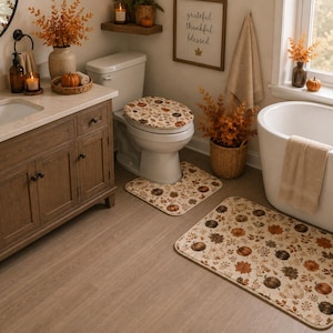 May include: A bathroom set featuring a toilet lid cover, a U-shaped contour rug, and a rectangular bath mat, all decorated with a repeating pattern of orange, brown, and cream pumpkins, autumn leaves, and small berries on a light beige background.